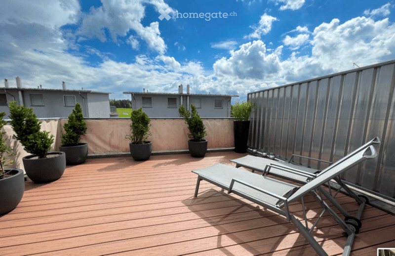 Roof terrace with wooden decking, lounge chairs, potted plants, and a view of neighboring buildings.