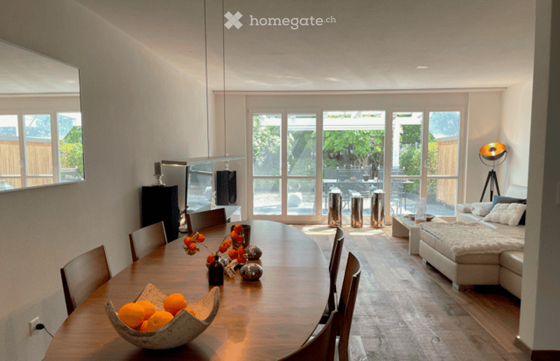 Open-plan living and dining area with modern furniture, large windows, and a view of the outdoor space.