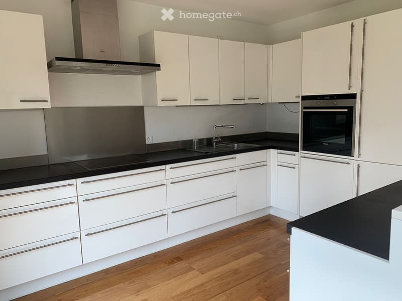 Modern kitchen with white cabinets, black countertops, and stainless steel appliances including a sink, faucet, and oven.
