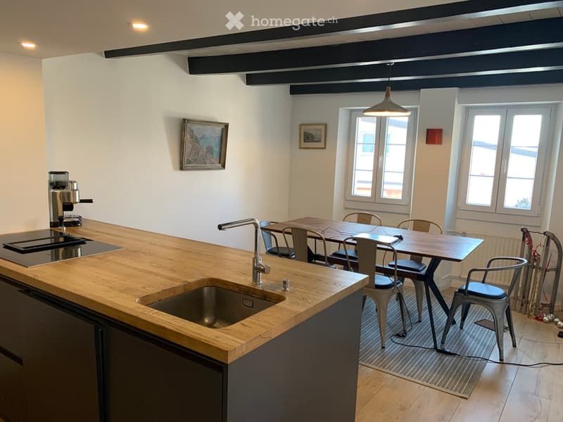 Modern kitchen with wooden countertops, stainless steel sink, coffee machine, and a dining area with a table and chairs.