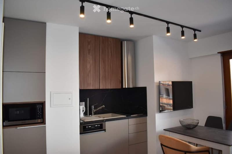 Modern kitchen and dining area with sleek wooden cabinets, stainless steel appliances, a sink, and a small dining table with chairs.