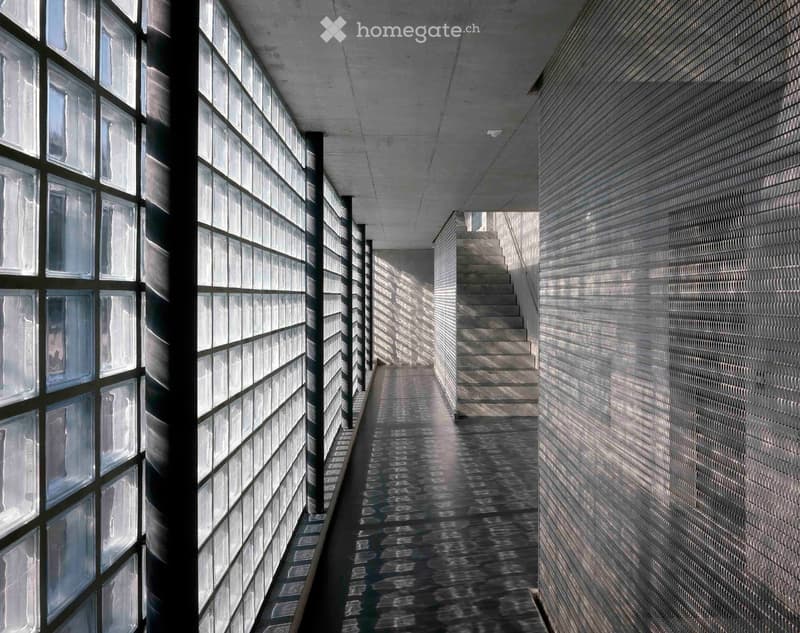 Modern corridor with glass block walls, polished concrete floor, and a staircase leading upwards.