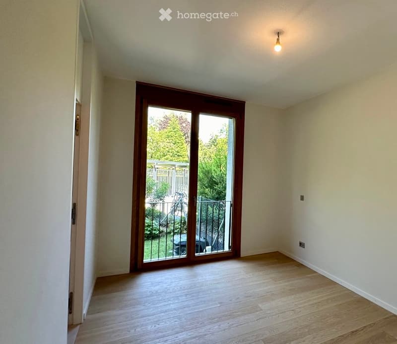 Empty room with wooden flooring, white walls, and a large sliding glass door leading to a balcony or outdoor area.