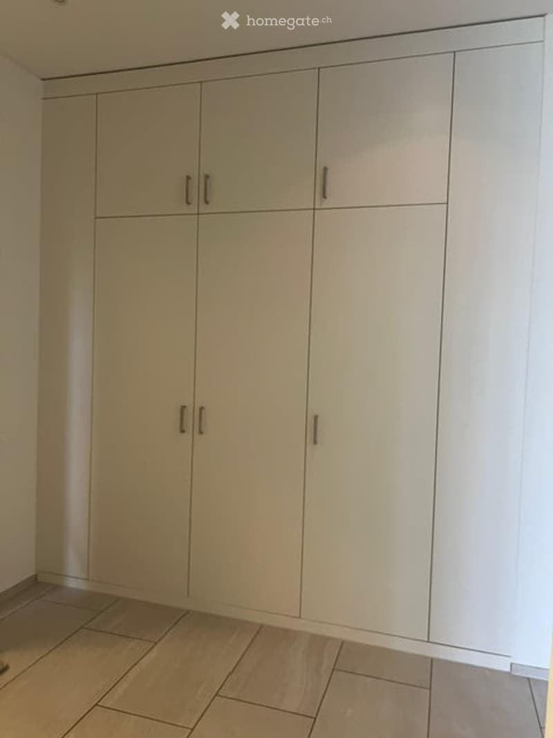 Empty room with light-colored built-in wardrobes and tiled flooring.