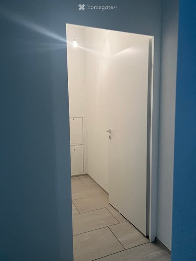 Empty hallway with tiled floor, white walls, and a closed white door at the end.