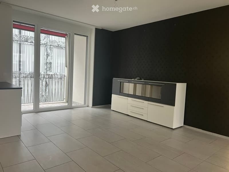 Modern, minimalist room with large glass doors leading to a balcony, white and black cabinet with mirror, tiled floor.