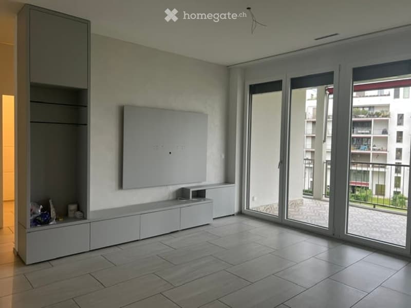 Empty room with large sliding glass doors leading to a balcony, white built-in cabinetry, and a flat-screen TV mounted on the wall.