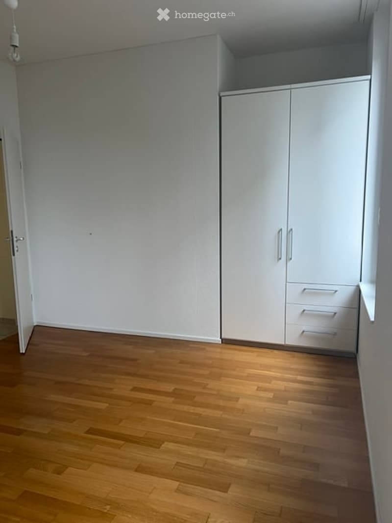Empty room with light wooden flooring, white walls, and built-in white closet with drawers.