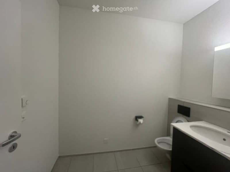 Modern bathroom with white walls, tiled floor, toilet, sink, and mirror.