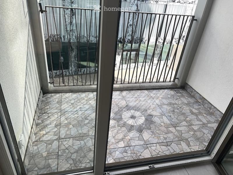 Balcony with tiled floor and metal railing, overlooking a green area.