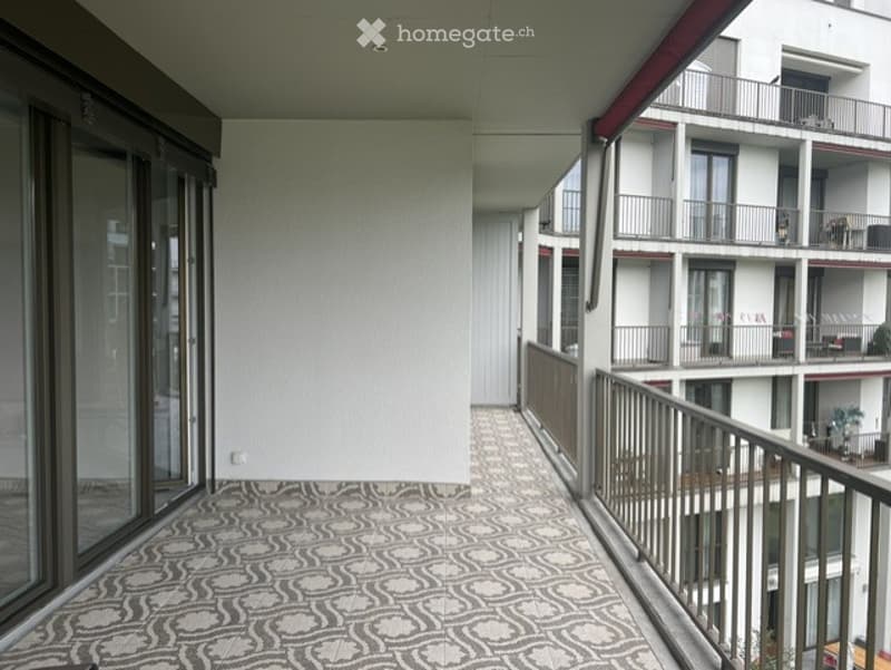 Balcony with patterned tile flooring, glass sliding doors, metal railing, and view of neighboring building.
