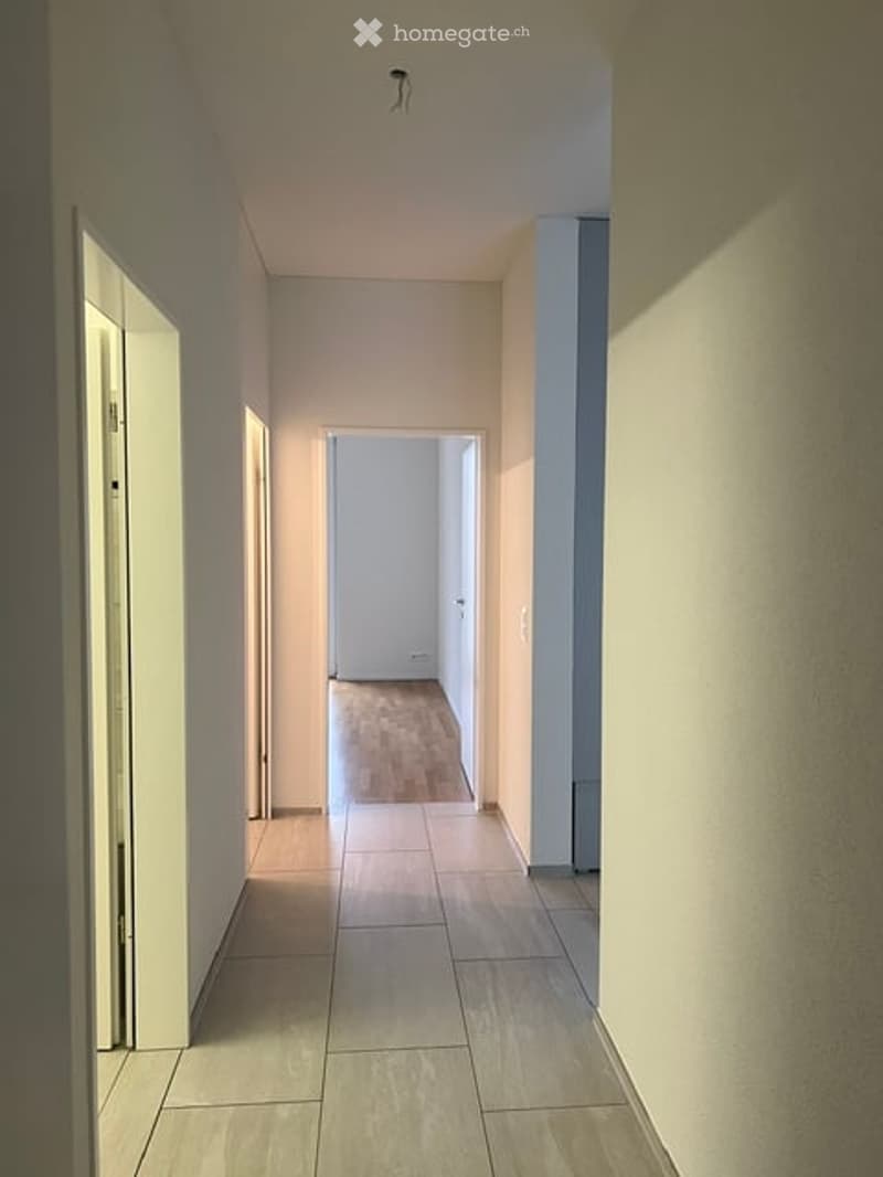 Empty hallway with tiled floor, white walls, and a closed door at the end.