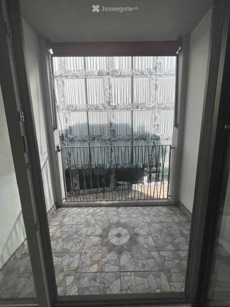 Balcony with tiled floor, metal railing, and a view of an adjacent building.
