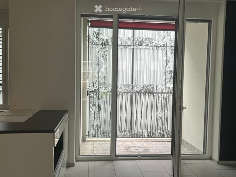 Empty room with a sliding glass door leading to a balcony or terrace. The room has a tiled floor and a small kitchen counter visible on the left side.