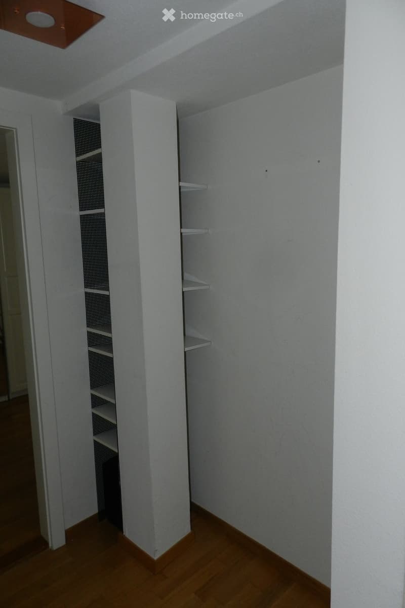 Empty room with wooden flooring, white walls, and built-in shelving units.