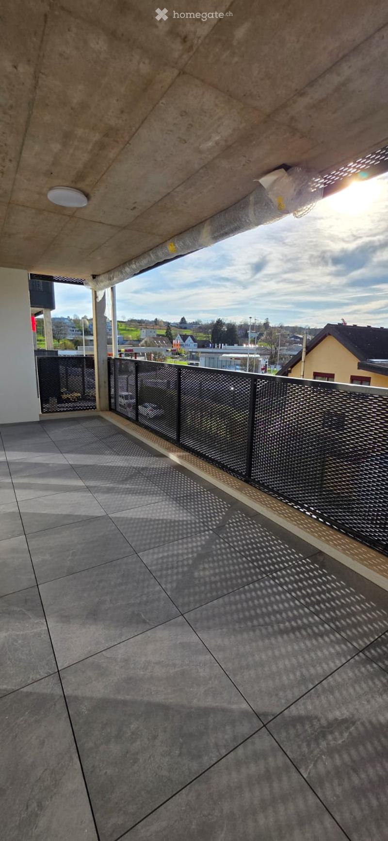 Empty balcony with tiled floor and metal railings, overlooking a cityscape.
