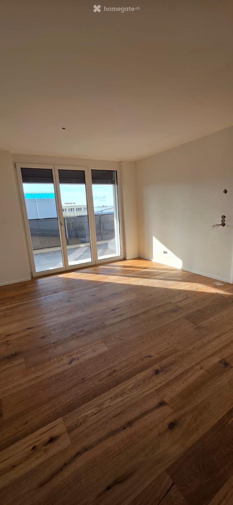 Empty room with hardwood floors, white walls, and large sliding glass doors leading to a balcony.
