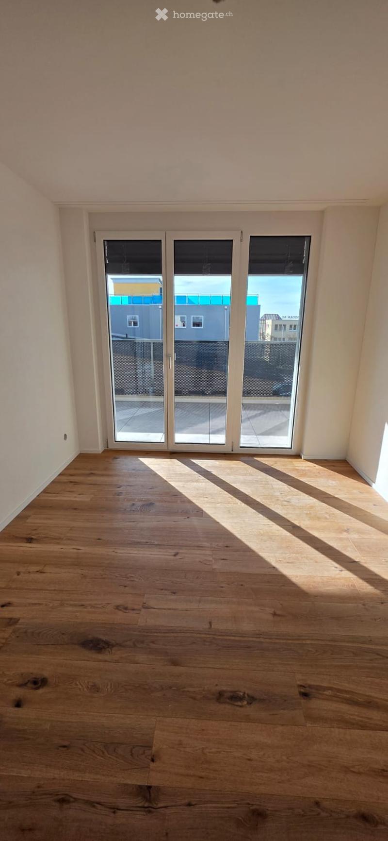 Empty room with wooden floors, white walls, and large sliding glass doors leading to a balcony.
