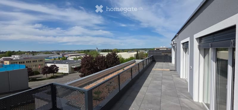 A balcony with a metal railing and a tiled floor, overlooking a cityscape with buildings and trees.