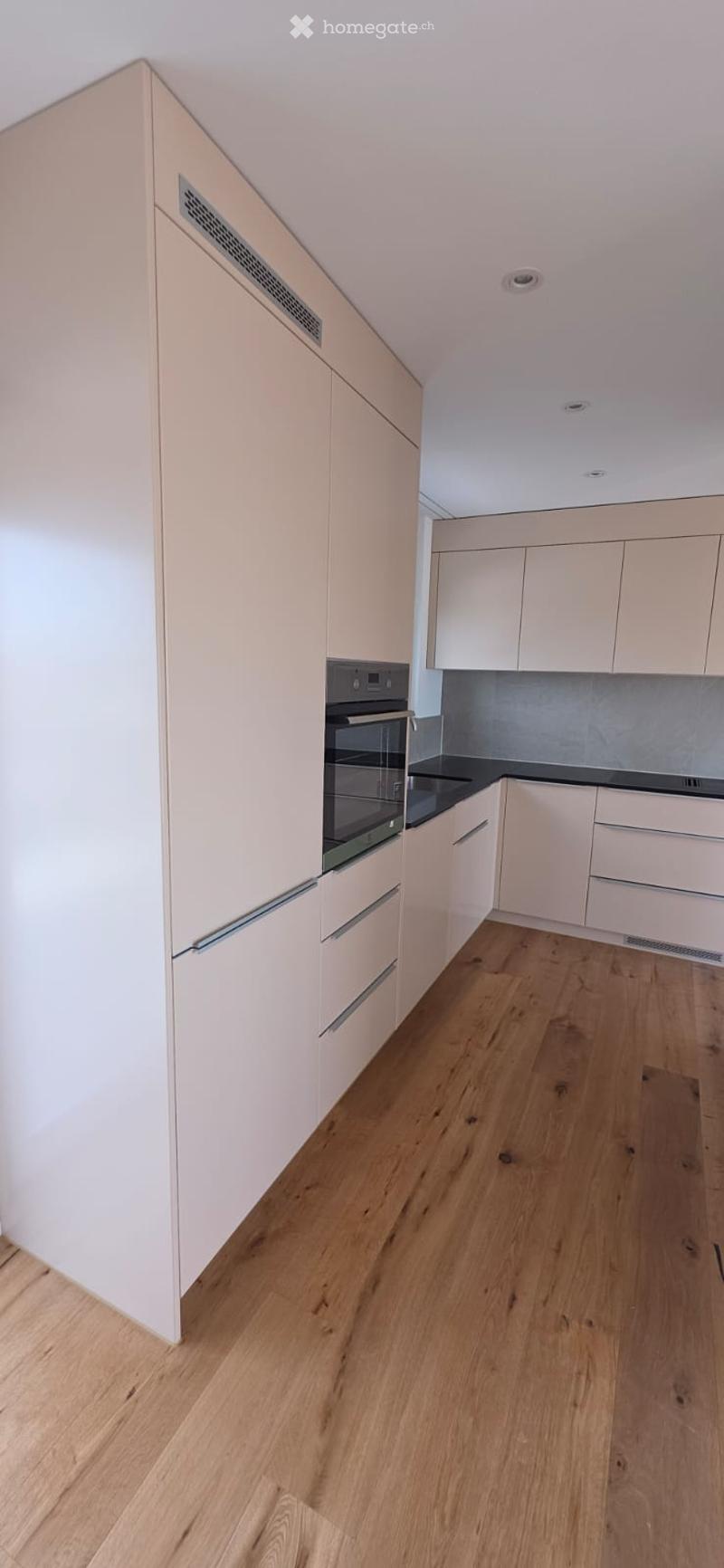 Modern kitchen with white cabinets, wooden floor, and black countertops. Integrated oven and sink.