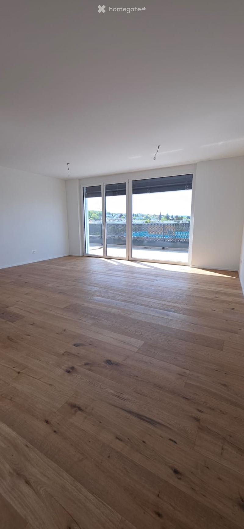 Empty room with hardwood floors, white walls, and large sliding glass doors leading to a balcony.