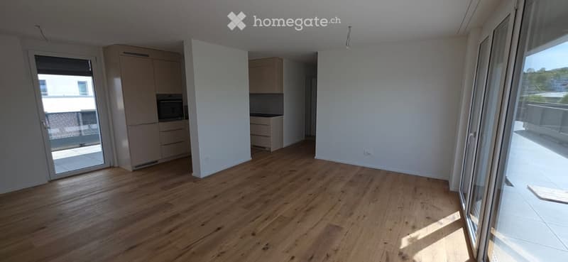 Empty room with wooden floors, white walls, and sliding glass doors leading to a balcony. There are built-in cabinets and a microwave in the kitchen area.