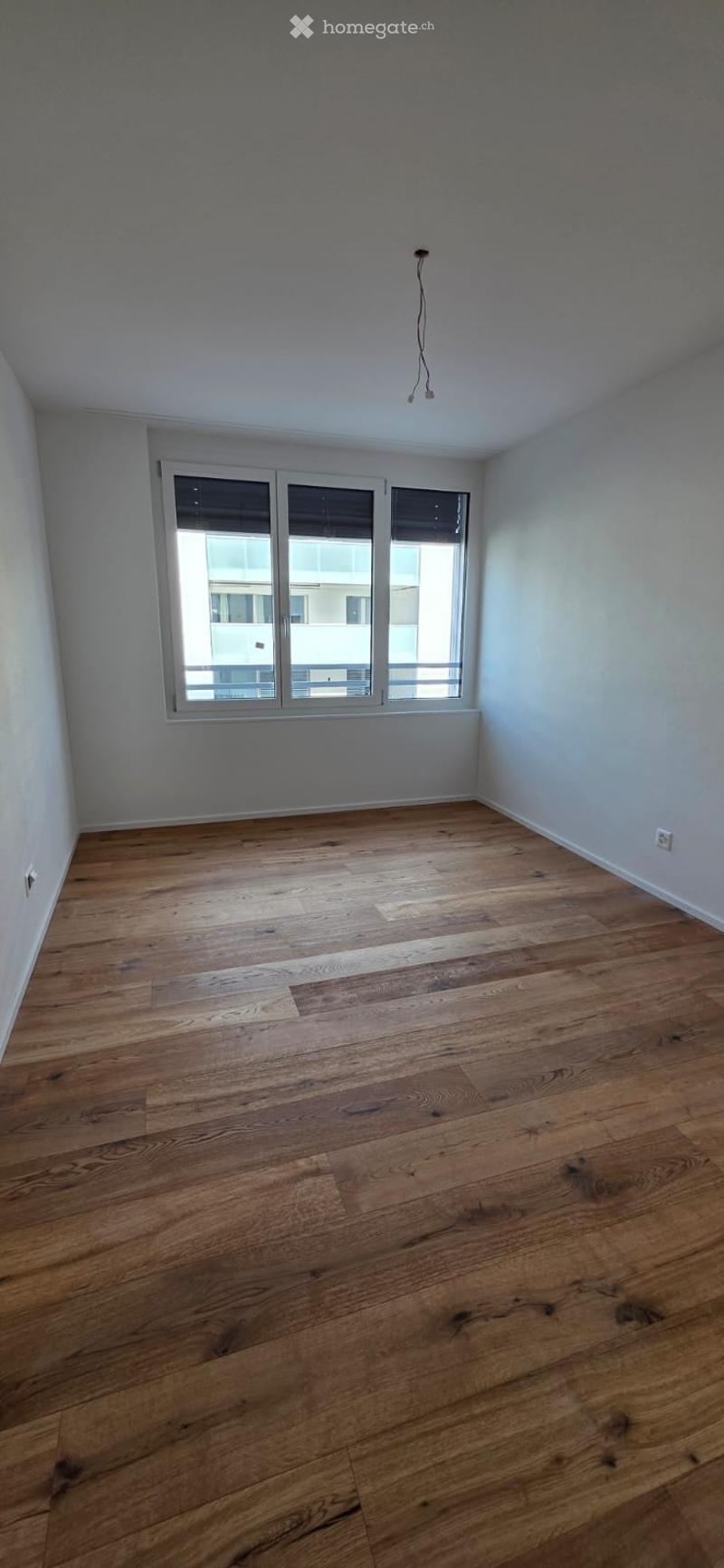 Empty room with hardwood floors, white walls, and large windows. No furniture or equipment.