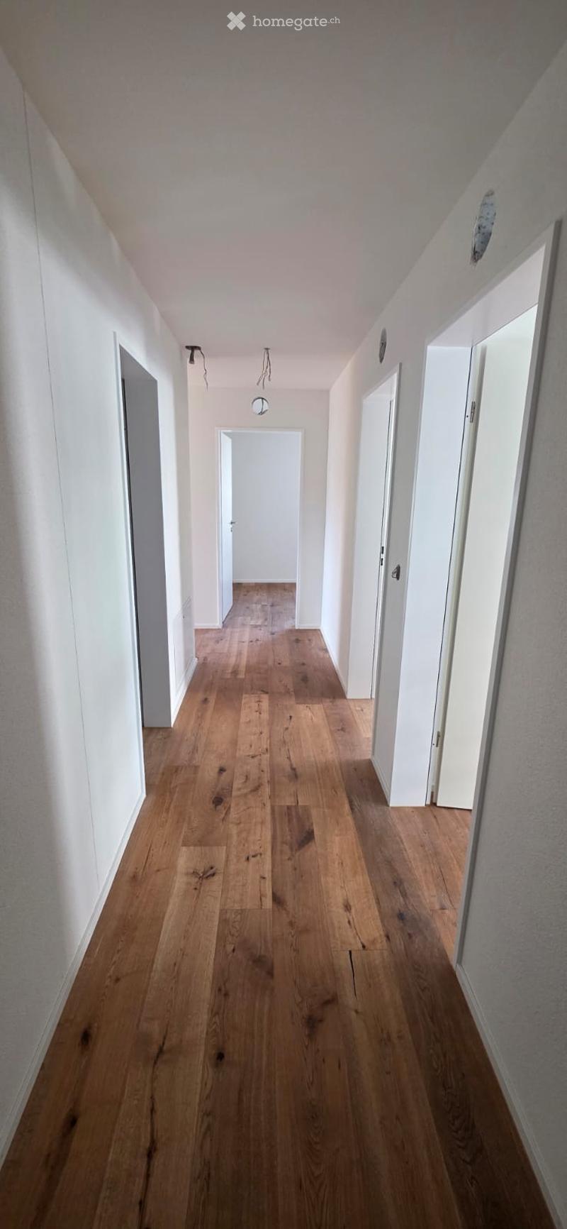 Empty corridor with wooden floors and white walls. Doors on both sides.