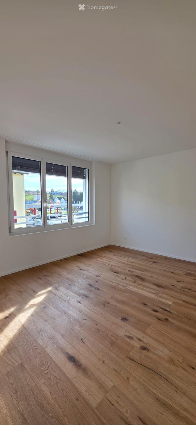 Empty room with hardwood floors, white walls, and large windows. No furniture or equipment.