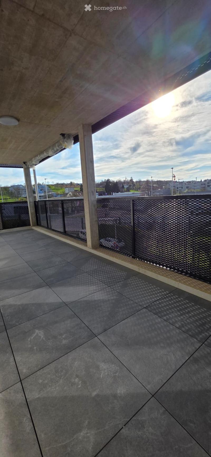 Empty balcony with tiled floor, metal railings, and a view of the city.