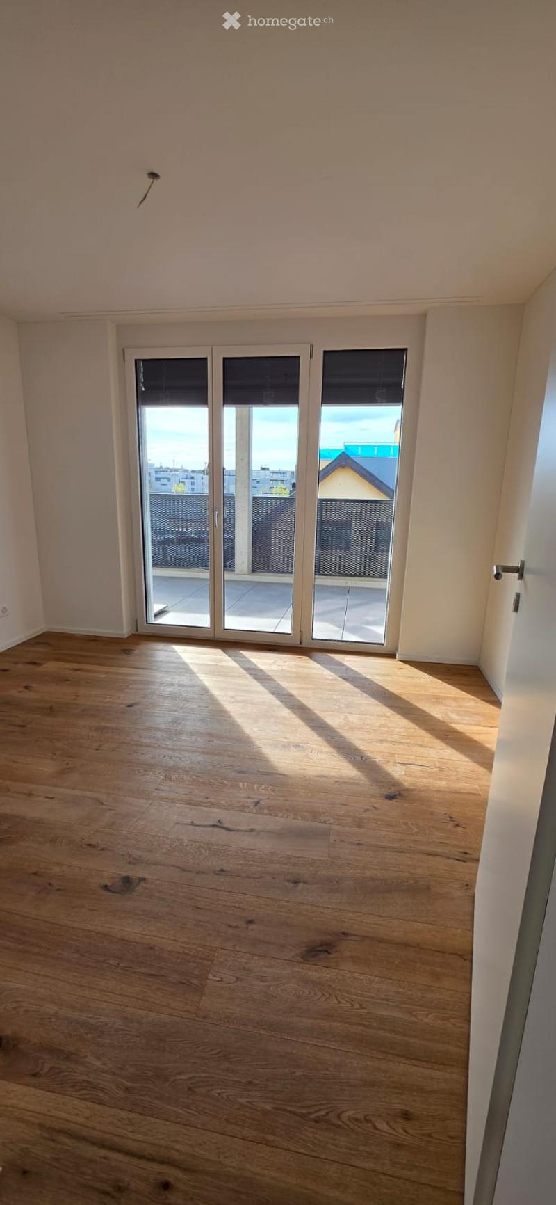Empty room with wooden floors and white walls. Large sliding glass doors lead to a balcony with a metal railing.