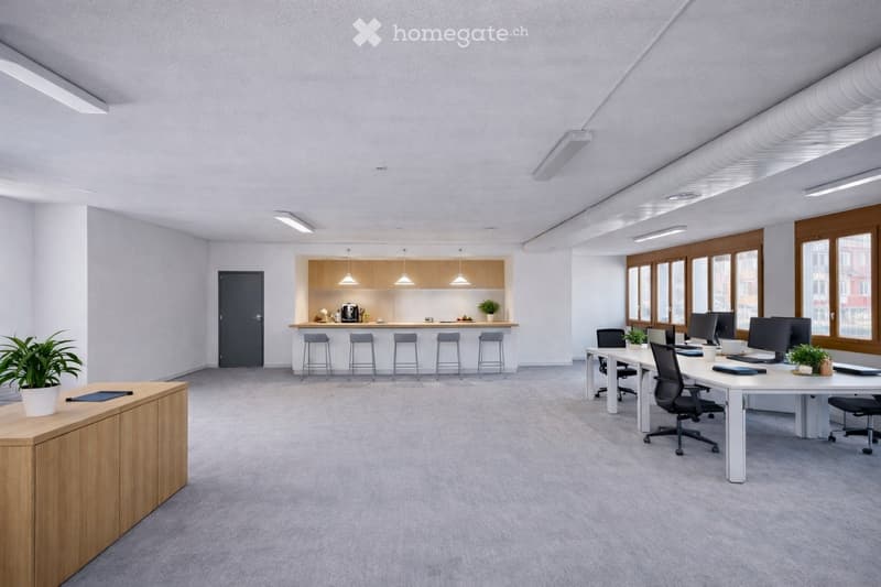 Modern office space with a large open area, featuring a kitchen area with a counter and stools, a reception desk with a plant, and a workspace with office tables, chairs, and computers.