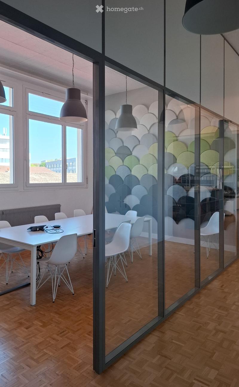 Modern office space with a long white table surrounded by white chairs, large windows, and glass partitions with decorative wall art.