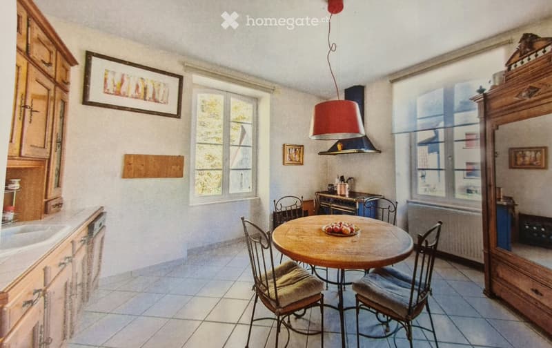 A cozy kitchen with wooden cabinets, a round wooden table with four chairs, a sink, and a window letting in natural light.