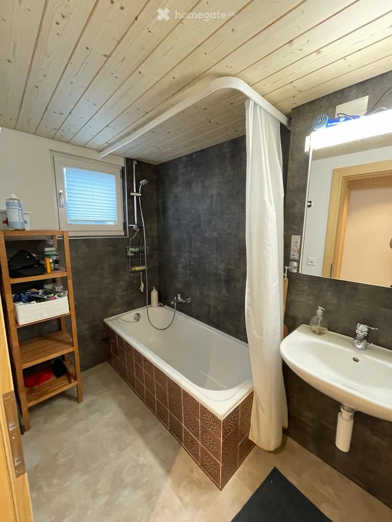 Bathroom with a bathtub, sink, mirror, shower curtain, and a wooden shelf holding various items.