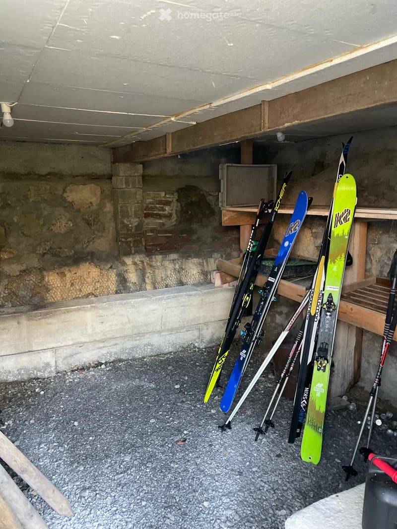 Underground storage area with concrete walls and ceiling, containing several skis and ski poles leaning against the wall.