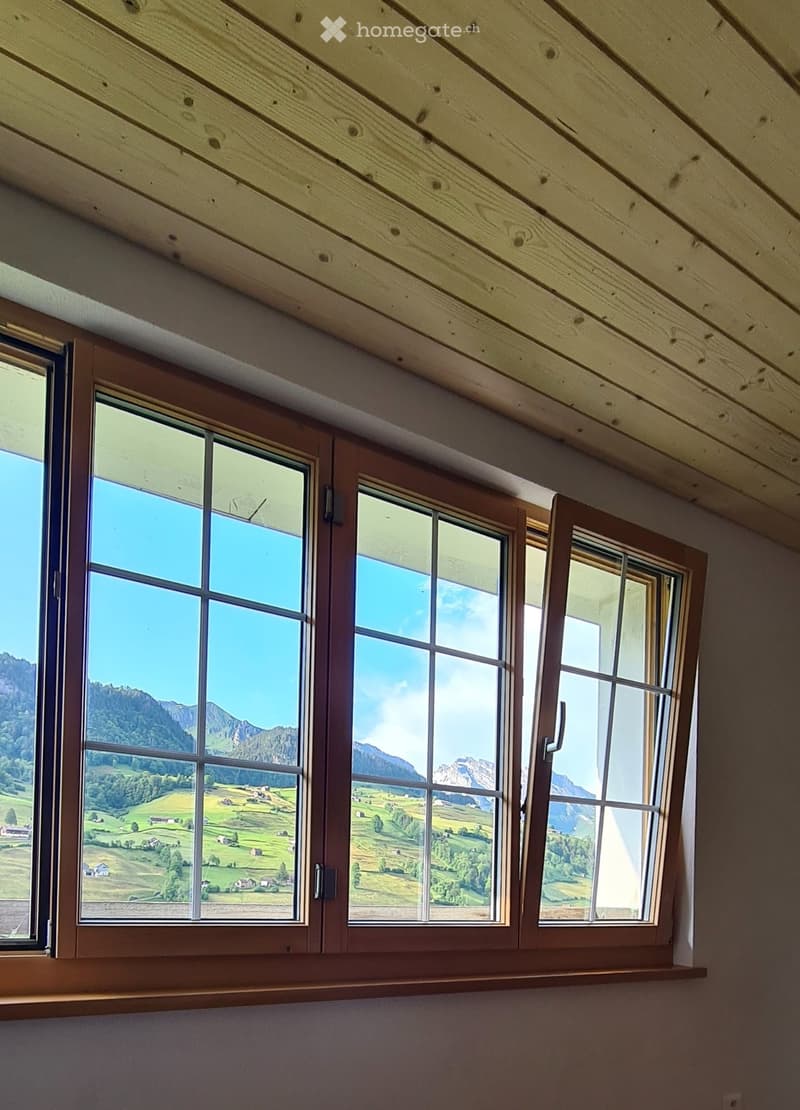 An unfurnished room with wooden slat ceilings and large windows offering a scenic mountain and valley view.