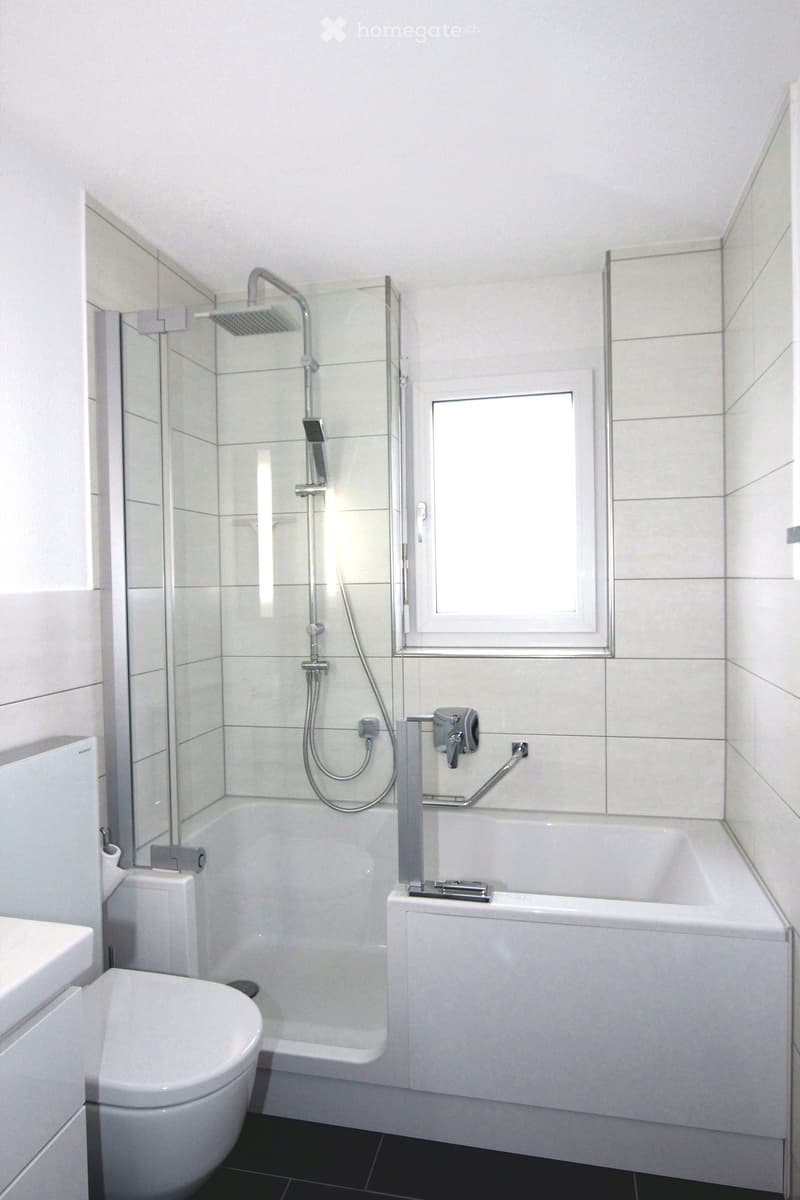 Modern bathroom with a bathtub, showerhead, toilet, and a window providing natural light.