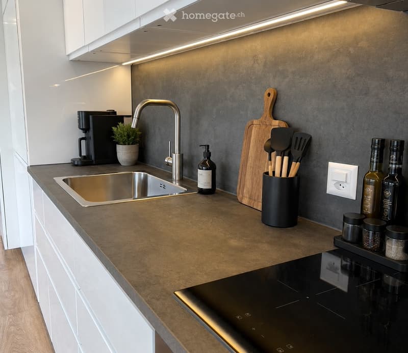 Modern kitchen with stainless steel sink, matte grey wall, white cabinets, and various appliances and utensils on the counter.