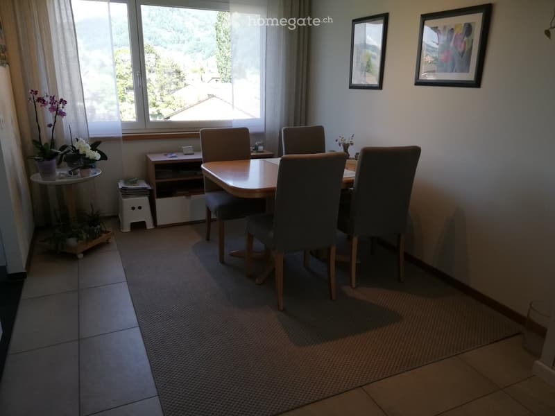 Dining room with a round wooden table, four chairs, side table with flowers, and artwork on the wall.