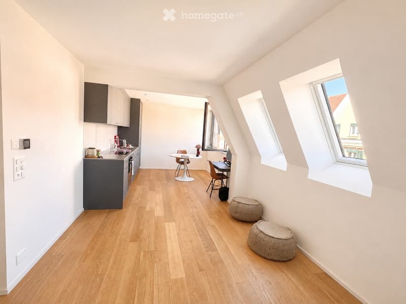 Bright, open-plan living and dining area with wooden flooring, modern kitchen, dining table, and two round woven stools.