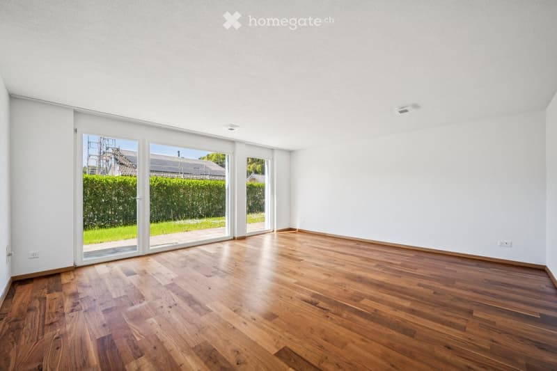 Empty room with wooden flooring, white walls, and large sliding glass doors leading to a green outdoor area.
