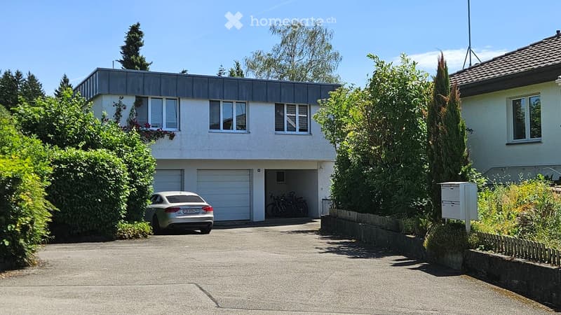 Two-story modern house with a flat roof, large windows, garage, and driveway with a parked car.