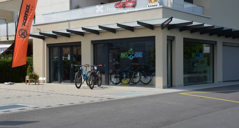 Modern storefront with large glass windows and awnings, displaying bicycles inside and outside, with signage reading "BIKE DIVE" and an orange banner.