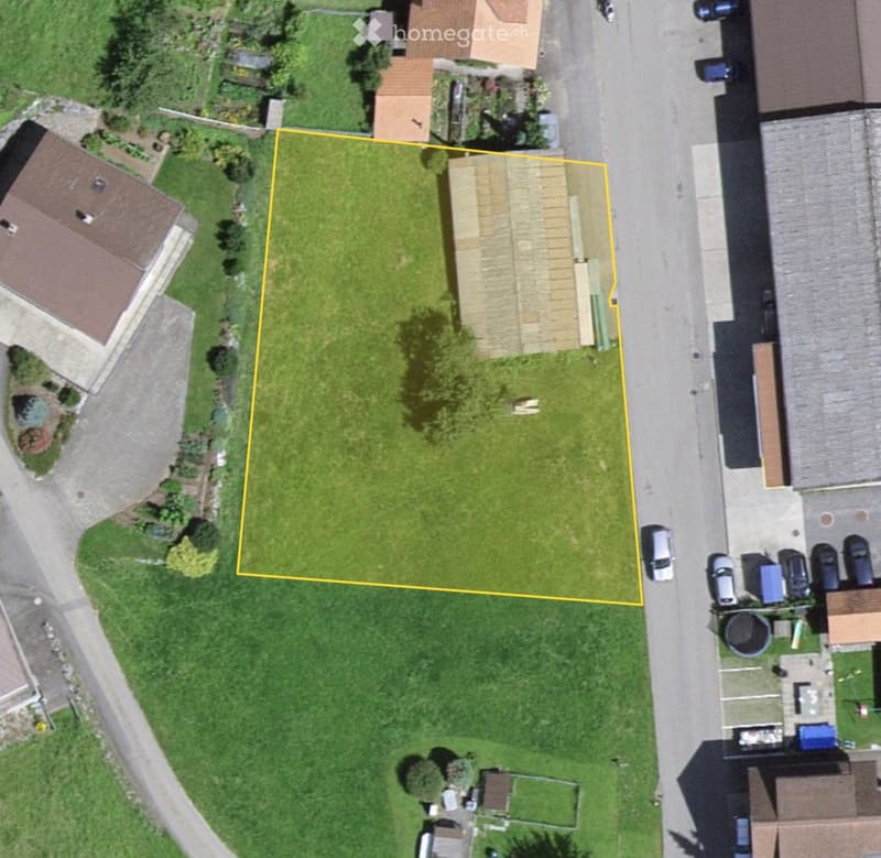 Aerial view of a residential area with a highlighted plot of land surrounded by neighboring houses, trees, and parked cars.