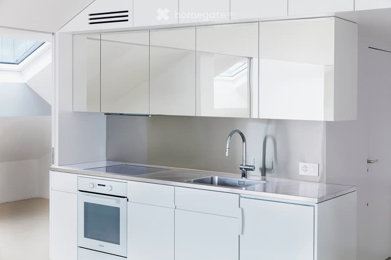 All-white kitchen with modern design, stainless steel sink, oven, gas stove, and cabinets, skylight window