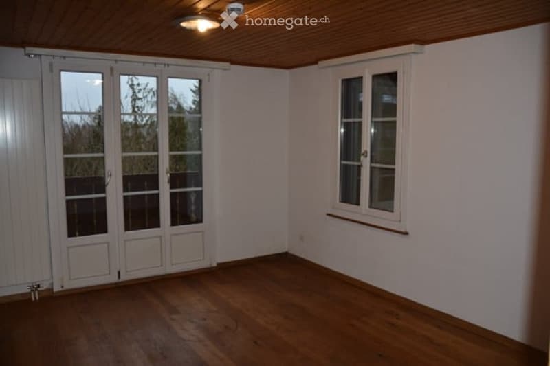 Empty room with wooden flooring, white walls, large sliding glass doors, and a single window with white frame.
