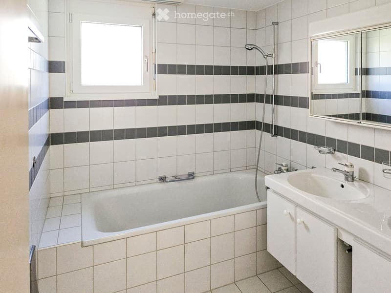 Modern bathroom with white tiles, a bathtub, a sink with a mirror, and a showerhead.