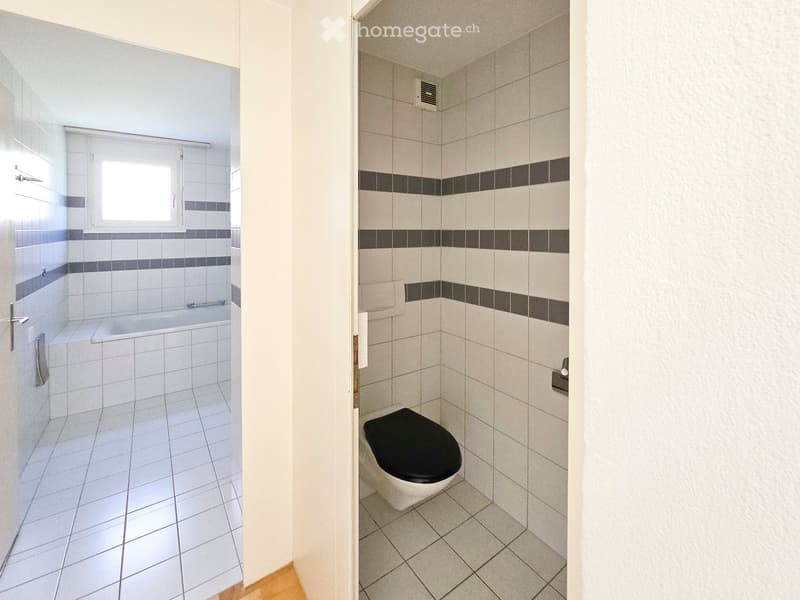 Modern bathroom with white tiles, black accents, and a bathtub in an adjacent space.
