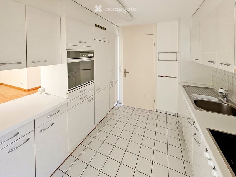 Modern kitchen with white cabinets, tiled floor, stainless steel sink, and built-in oven.